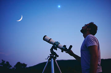 Man with telescope looking up at evening sky