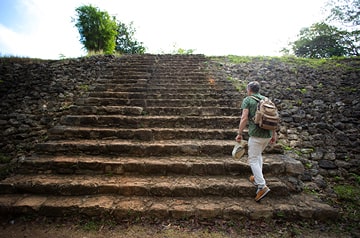 A white man in a backpack climbs a set of stone steps.