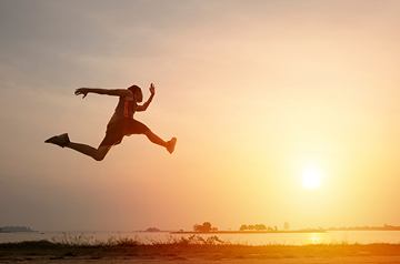 Person leaping in a field at sunset