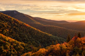The sunrise lighting up clouds behind a series of hills.