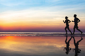 Two people jogging along a beach at sunset