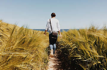 A person walking towards the beach through tall grass