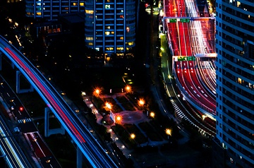 Nighttime cityscape with bright skyscrapers and colorful light trails on busy highways.