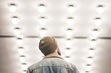 A man in a denim jacket and beanie standing under a hallway lined with lights
