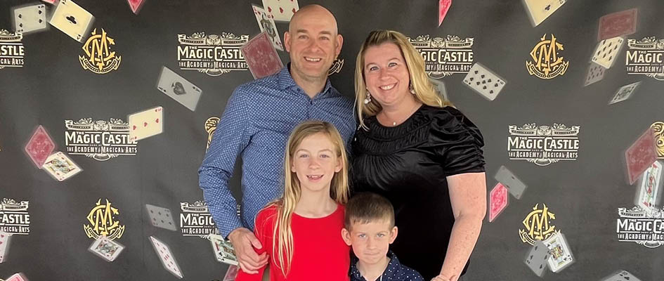 Cheryl Teeter-Balin standing with a man and two children in front of a Magic Castle backdrop.