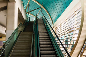 Looking up a set of stairs towards a green glass ceiling.