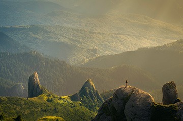 Hiker on rocky outcrop looking at mountain valley