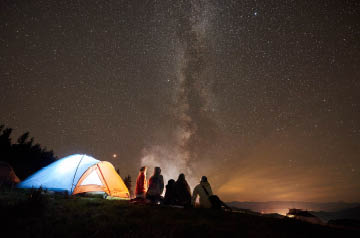 Nightscape with group of people around a campfire and tents glowing