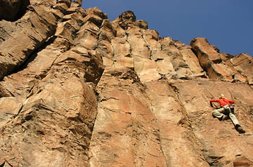 Looking skyward along a cliff face with a climber scaling the rocks