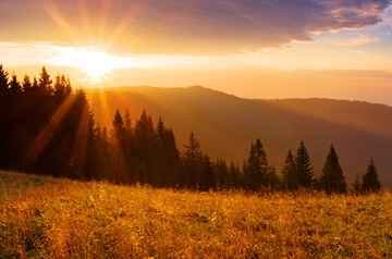 Looking across a meadow and trees to sunrise over two hills