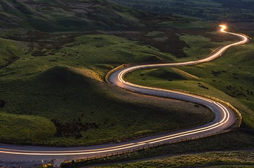 Headlights on a highway winding through green hills.